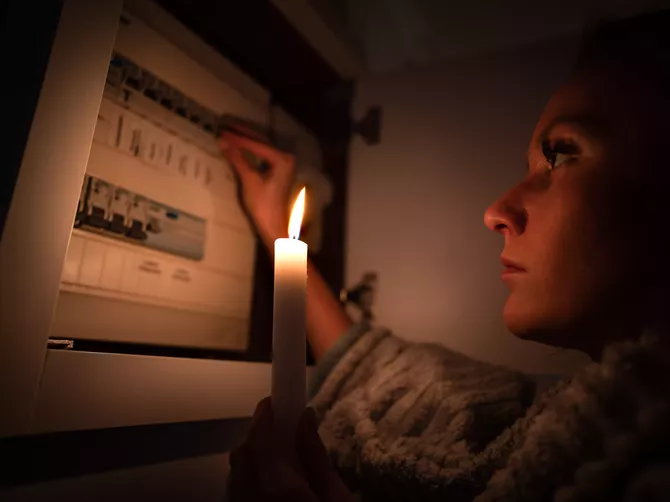 Kvinna i mörker med stearinljus i handen. Undersöker elcentral.