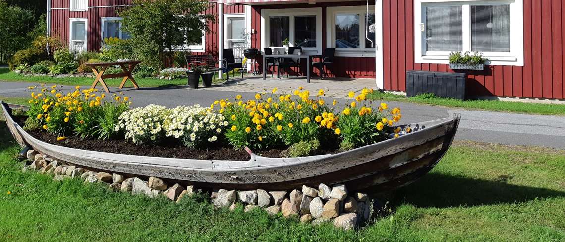 Tallgårdens äldreboende. Båt med blommor, bord och stolar, blommor och buskar utanför huset.