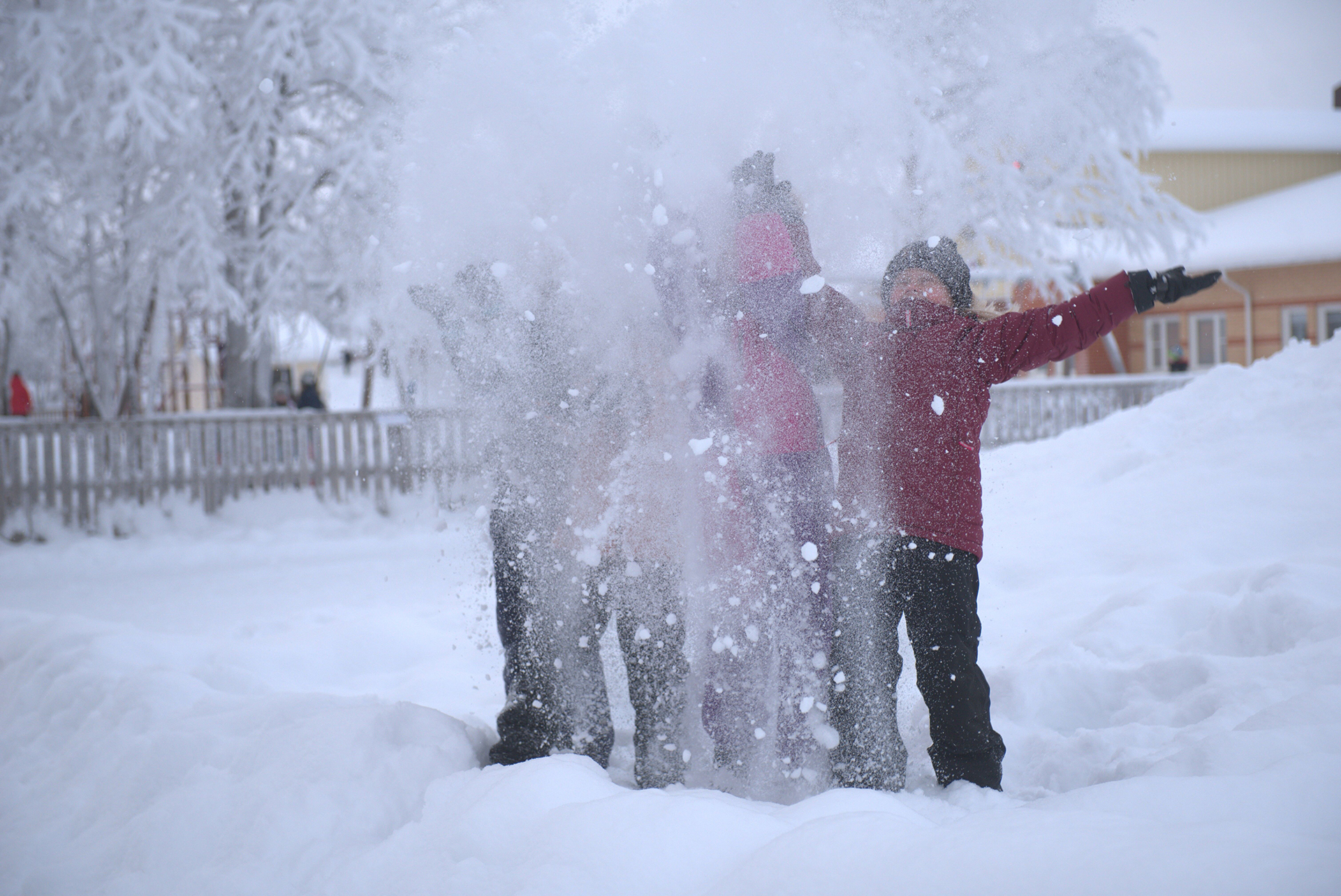 En grupp barn står ute i snön och kastar upp snö som bildar ett vitt moln framför dom