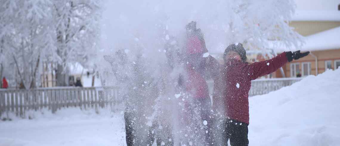 En grupp barn står ute i snön och kastar upp snö som bildar ett vitt moln framför dom